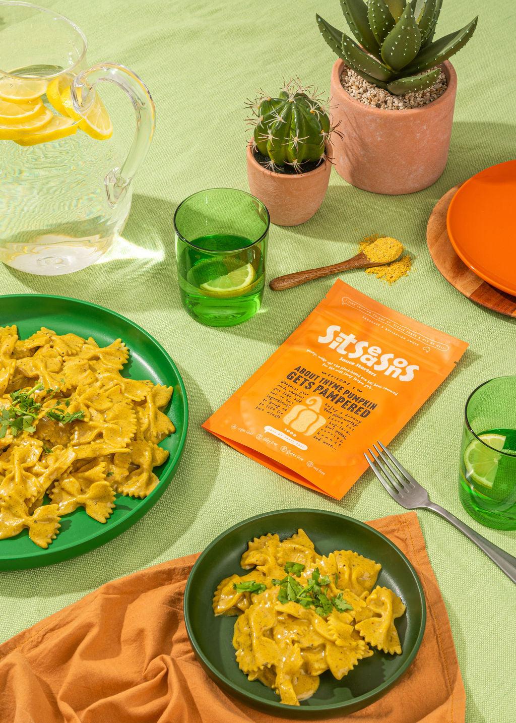 Two plates of vegan pumpkin Alfredo pasta with an orange sauce packet